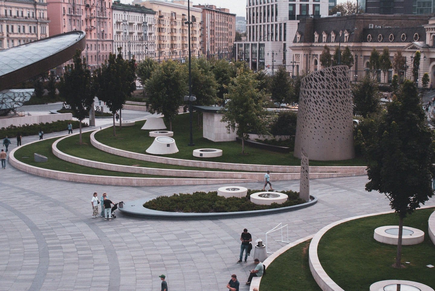People walking through a modern urban plaza with landscaped grass.